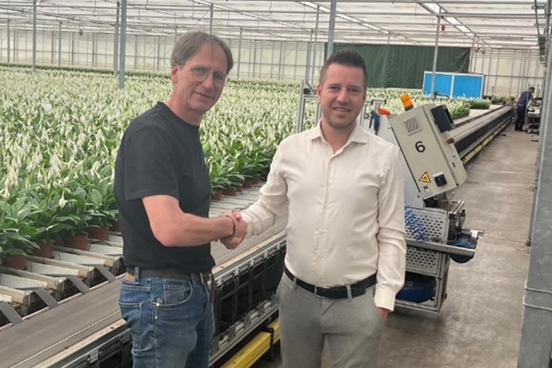 Twee heren schudden elkaar de hand in een kas met planten op de achtergrond