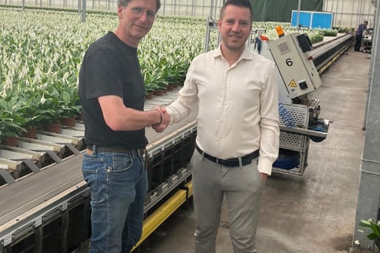 Twee heren schudden elkaar de hand in een kas met planten op de achtergrond